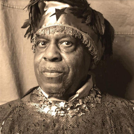 Black and white image of Sun Ra wearing a traditional headpiece and ornate clothing.