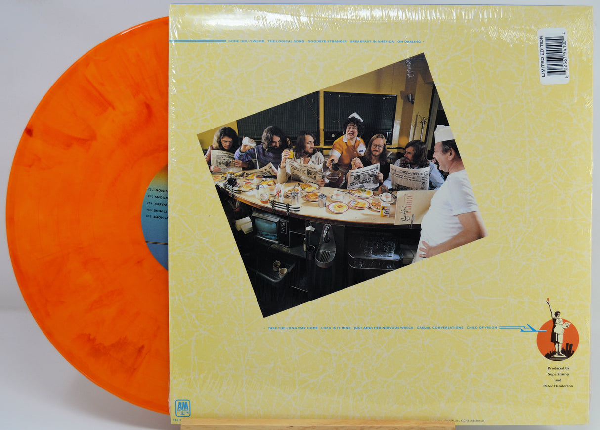 Vinyl record LP partially pulled from its cover, showing a translucent orange record and a pale yellow cover with a central photo print of a group dining at a table.