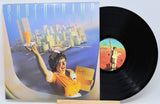 Vinyl record with a colorful cover featuring a person and cityscape, on a white background.