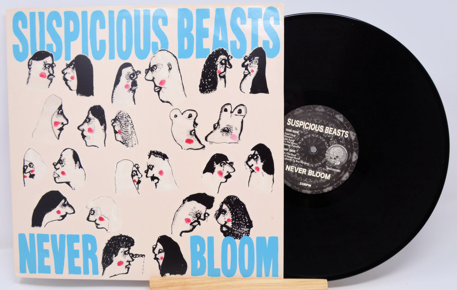 Vinyl record with 'Suspicious Beasts' cover featuring illustrations of stylized faces.