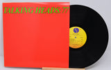 A vinyl record titled 'Talking Heads - 77' with a red cover and a black record inside. The label shows the band name and the album title.