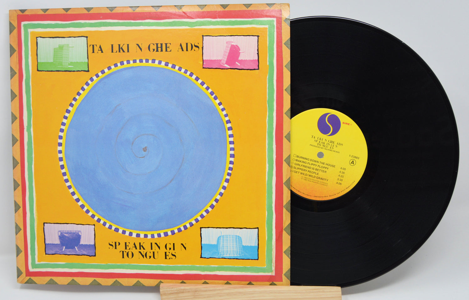 Vinyl record and cover for the album 'Speaking In Tongues' by Talking Heads, featuring a blue circle on a yellow background with various icons around it.