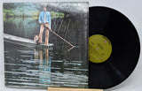 Vinyl record with a cover showing a person and dog on a dock, against a natural background.