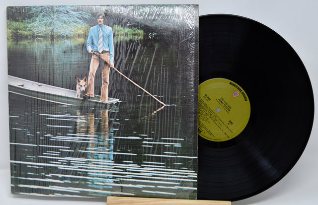 Vinyl record with a cover showing a person and dog on a dock, against a natural background.