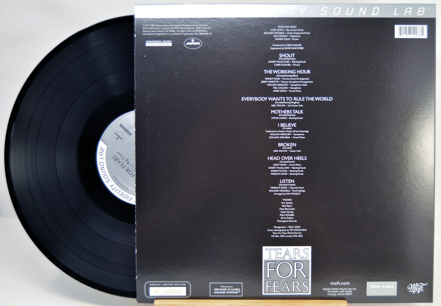 A vinyl record partially pulled from its sleeve, showing the back of the packaging. The black record is visible on the left, and the sleeve is black with white printed tracklist text and the title 'TEARS FOR FEARS' near the bottom.
