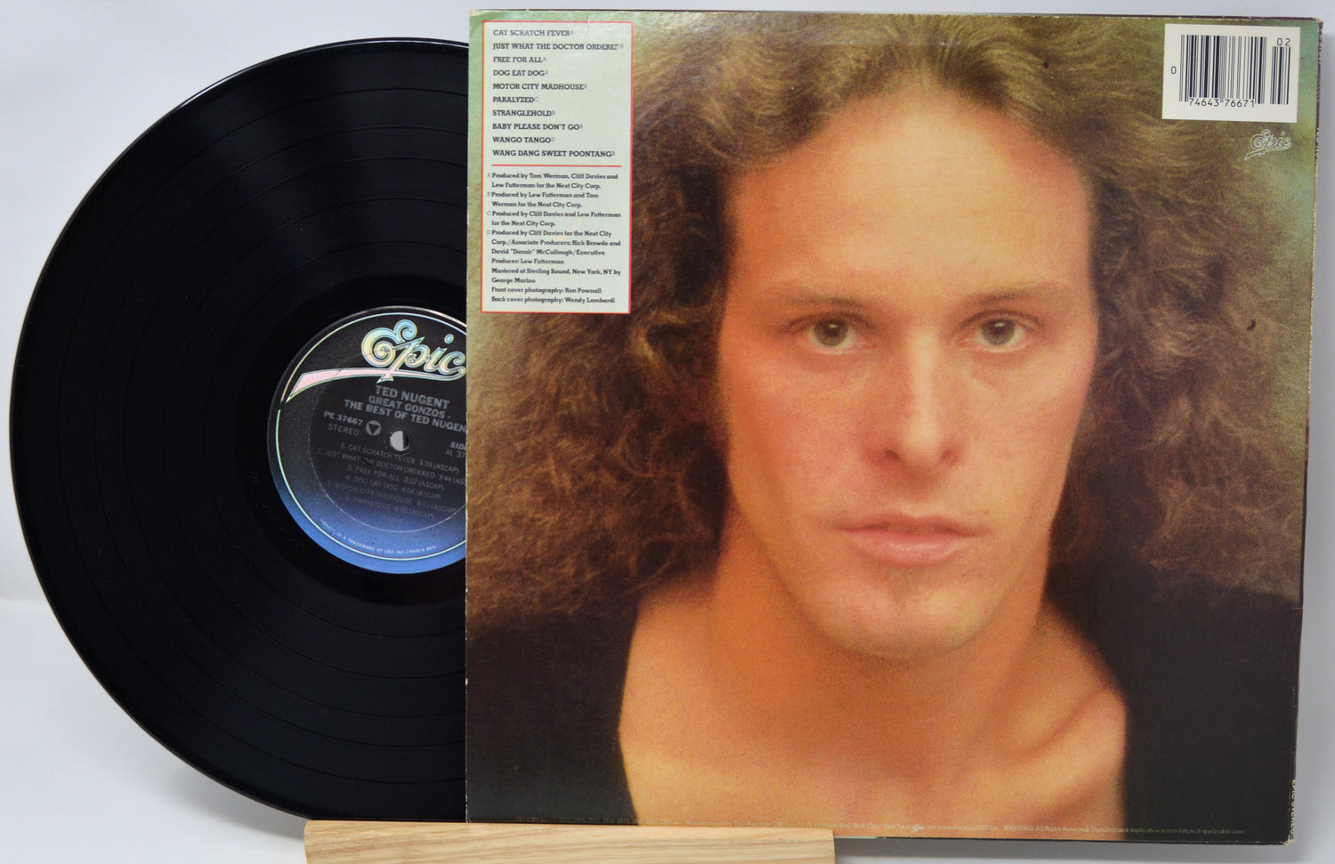 A vinyl record partially pulled from its album cover, showing the black LP disc and the printed back cover with a portrait of a man and track listing text.