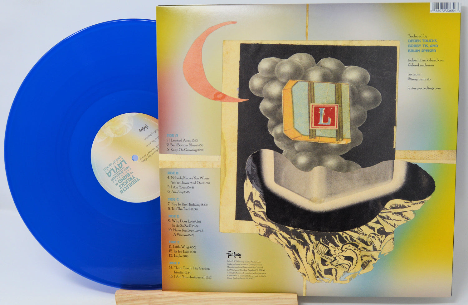 A vinyl record partially pulled from its album sleeve, showing a bright blue record with a cream label next to the illustrated back cover.