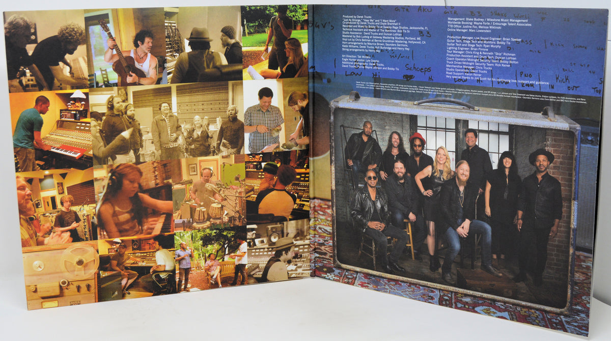 A printed booklet or album insert shown open on a white surface, with a collage of band photos on the left page and a large group photo inside a suitcase graphic on the right page.
