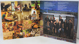 A printed booklet or album insert shown open on a white surface, with a collage of band photos on the left page and a large group photo inside a suitcase graphic on the right page.