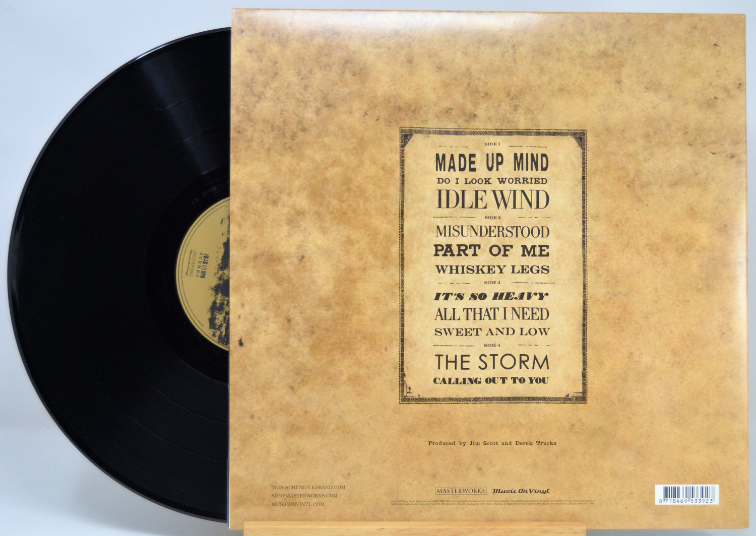 A vinyl record partially pulled from its sleeve, showing the black record on the left and the tan paper sleeve on the right. The sleeve features a vintage-style aged paper texture with a black-bordered tracklist for the album.