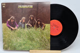 Vinyl record with cover featuring a band sitting in grass, on a light blue background