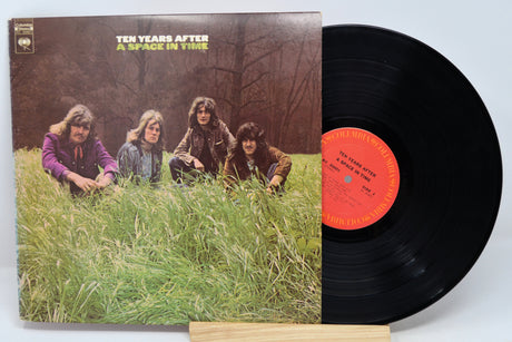 Vinyl record with cover featuring a band sitting in grass, on a light blue background