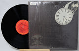 Vinyl record with a black cover featuring a clock and a hand, on a white background.