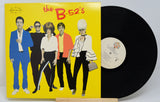 The image shows a vinyl record of 'The B-52's' with a yellow album cover featuring black and white band photo. The record is placed on a wooden platter.