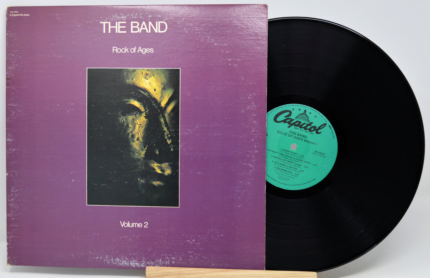 The Band's 'Rock of Ages Volume 2' vinyl record LP, showing the purple cover sleeve with the album artwork and the black record partially pulled out, revealing the green Capitol label.