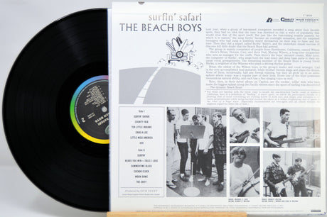 Vinyl record album shown with the black LP partially pulled from the printed inner sleeve. The sleeve features the title 'surfin' safari', the band name 'THE BEACH BOYS', track list, and black-and-white photos of the band members.