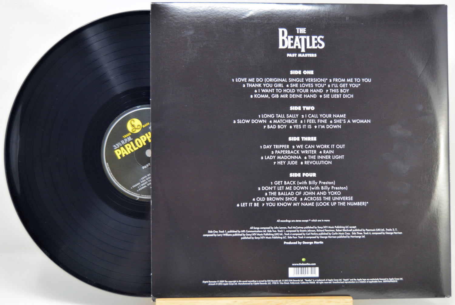 The Beatles - Past Masters vinyl record shown with the black LP partially pulled from the back of the outer paper sleeve. The sleeve displays the band's name and track listing in white text on a black background.