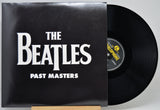 The Beatles 'Past Masters' vinyl record with the black album cover and part of the black record visible, photographed against a light gray background.