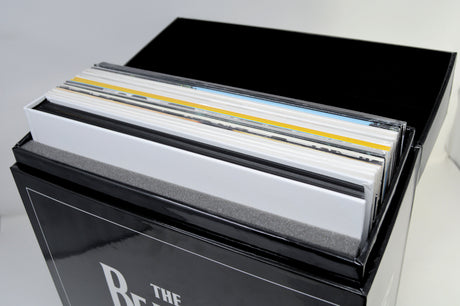 A close-up of a black vinyl record box with several records partially pulled out, showing the record sleeves and spine edges in white, black, yellow, and blue. The front of the box shows the partial text 'The Beatles'.