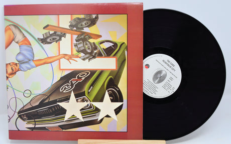 The image shows a vinyl record and cover for the album 'Heartbeat City' by The Cars. The cover features a illustration of a car and stars.