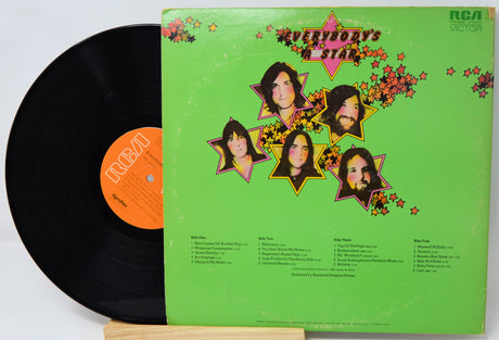 Vinyl record with a green cover featuring star designs and faces, on a white background.