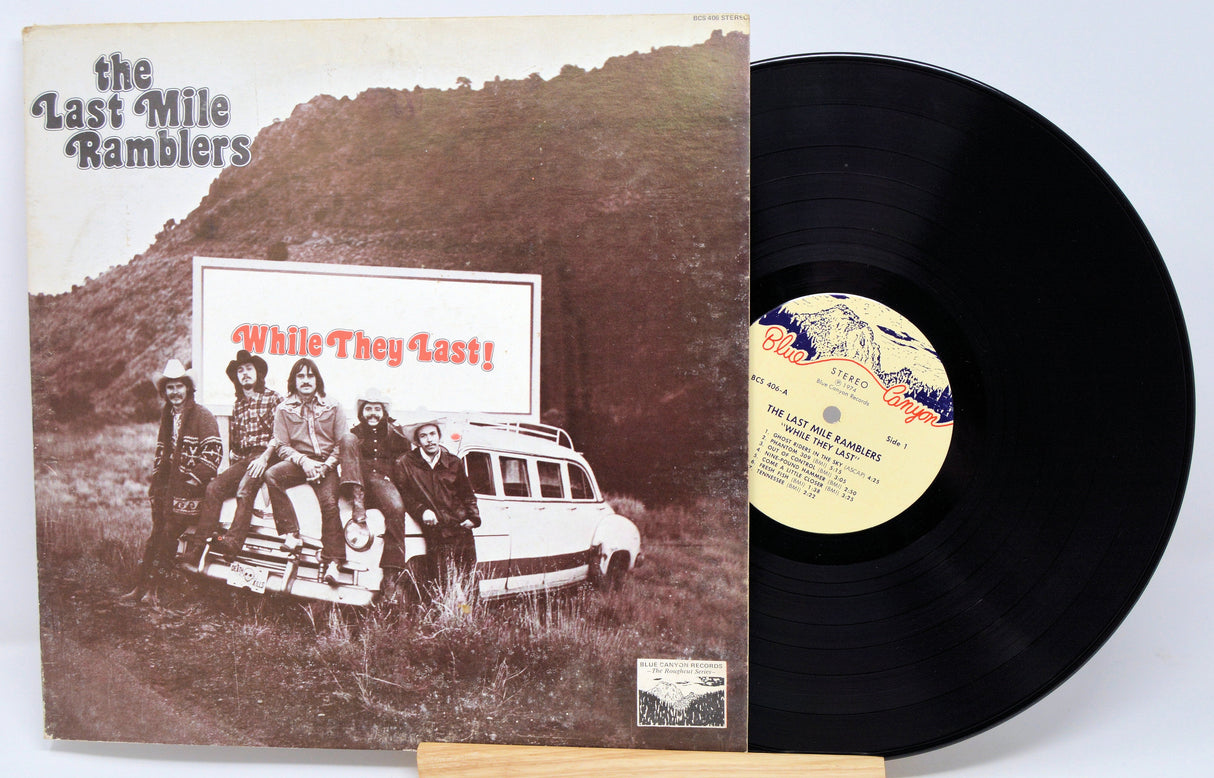 Front cover of The Last Mile Ramblers – While They Last! vinyl LP, featuring the band by a vintage car and album title