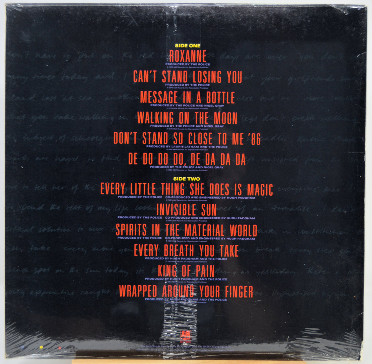The back cover of a vinyl record featuring a black background with the tracklist printed in red and yellow text, wrapped in clear plastic.