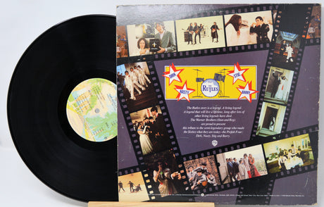 A vinyl record partially pulled from its printed paper sleeve. The black record has a light-colored center label, and the sleeve features a collage of photos arranged like a film strip with a purple background and a yellow band labeled 'The Beatles'.