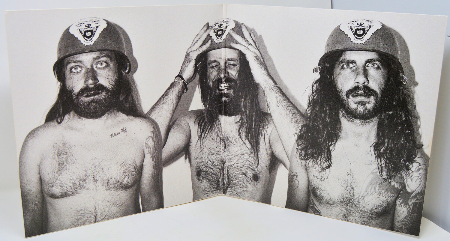 Black and white photo of three long-haired men wearing helmets with wolf emblem, inside vinyl gatefold