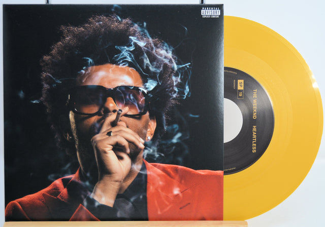 The Weekend Heartless variant #10 7 Inch Vinyl record with a black front cover featuring a person wearing sunglasses and a red jacket, and a yellow record inside.