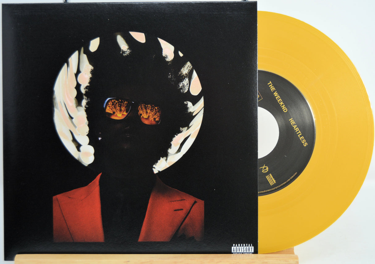 The Weekend Heartless variant #5 7 Inch Vinyl record with a black front cover featuring a person wearing sunglasses and a red jacket, and a yellow record inside.