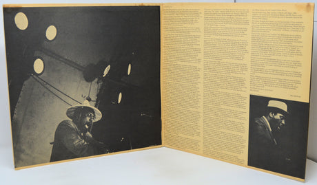 An open vintage book or magazine spread, showing a large black-and-white photograph on the left page and columns of text on the right, with a small inset portrait near the bottom right. The pages are cream-colored with dark printed content.