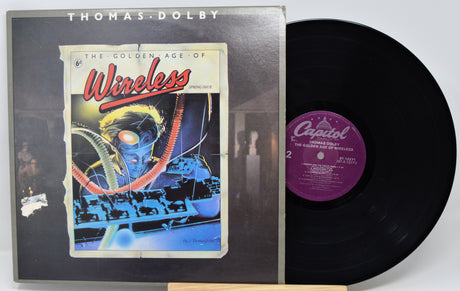 Thomas Dolby's 'The Golden Age of Wireless' vinyl record album shown with its outer jacket and the black record partially pulled out. The album cover features a colorful sci-fi illustration, and the record label is Capitol Records.