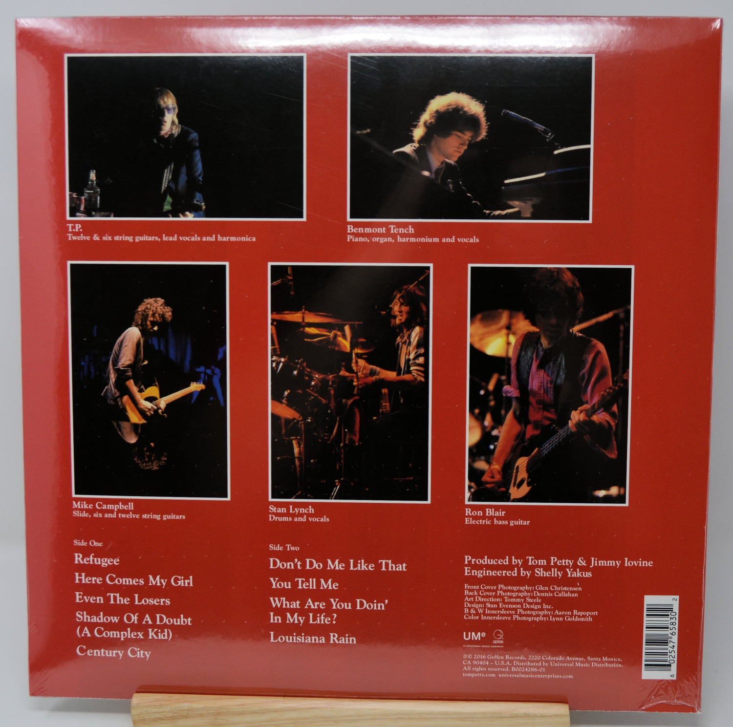 The back cover of a vinyl record sleeve, featuring a solid red background with five black-and-white concert photos of musicians, track listings, and credits on a wooden display stand.