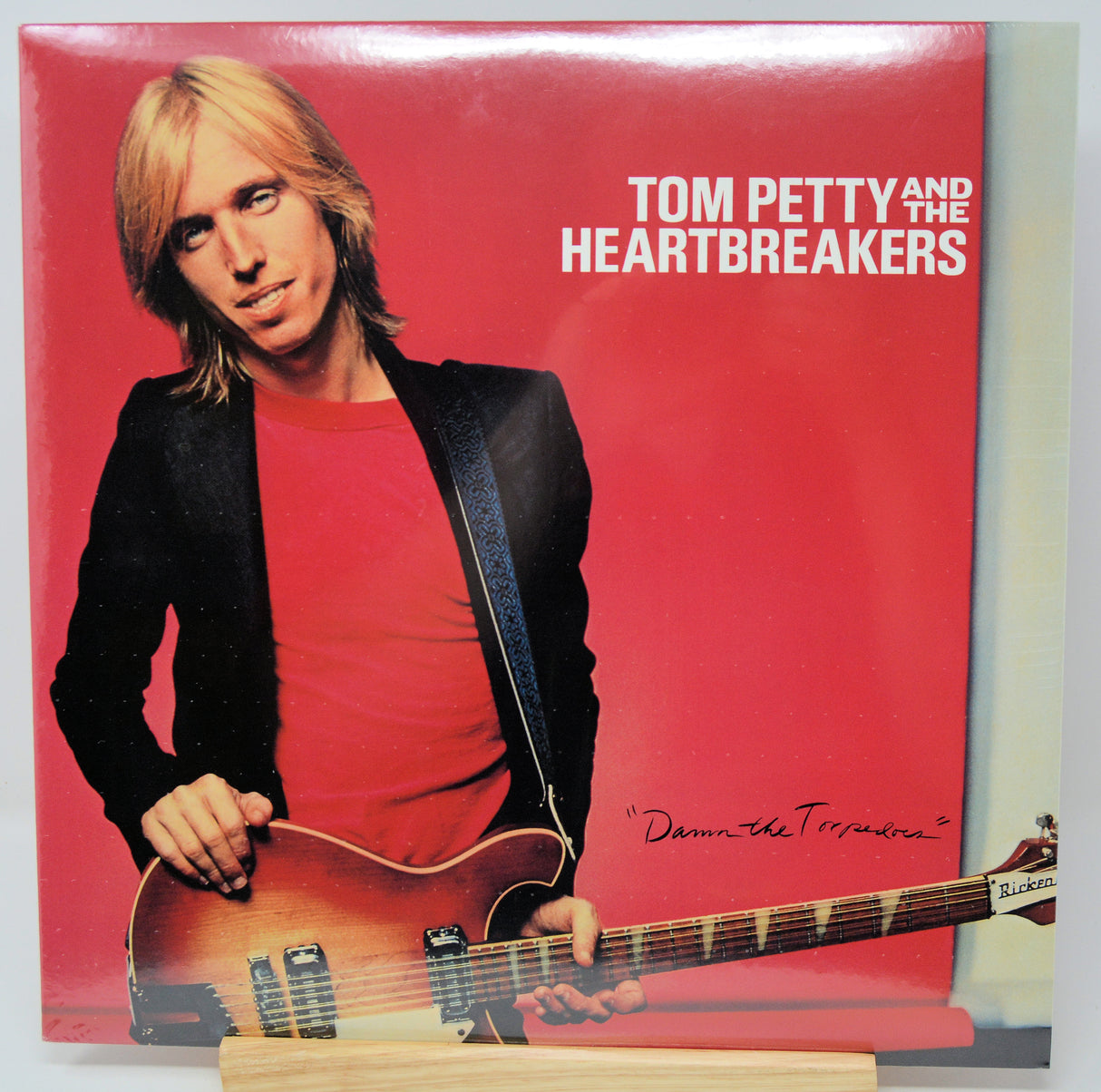 Tom Petty and the Heartbreakers vinyl record cover, featuring a blonde man in a black blazer and red shirt holding an electric guitar against a bright red background.