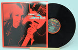 Vinyl record with cover featuring Tom Petty holding a guitar, on a red background.