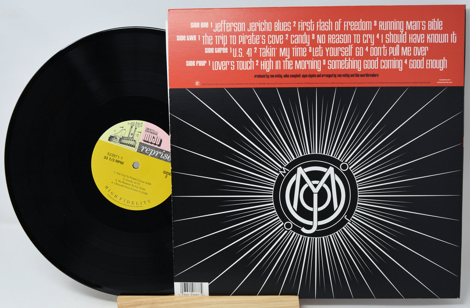A vinyl record partially pulled from its sleeve, showing the black record, a yellow center label, and the back cover with a red header and black-and-white sunburst design.