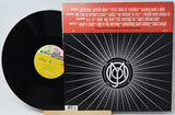 A vinyl record partially pulled from its sleeve, showing the black record, a yellow center label, and the back cover with a red header and black-and-white sunburst design.