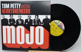 Tom Petty and the Heartbreakers 'Mojo' vinyl record album with the black LP record partially pulled from the sleeve, photographed on a light gray background.