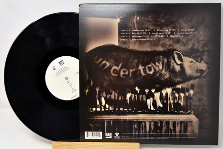 A vinyl record partially pulled from its sleeve, showing the black record on the left and the back cover of the album on the right. The sleeve features a dark sepia-toned photo of a pig with the word 'uncertain' written across it, plus track listing text at the top.
