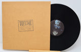 Vinyl record with a brown sleeve featuring a logo on a light gray background