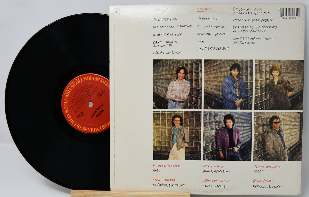 A vinyl record partially pulled from its back cover sleeve, showing the black record on the left and the printed back of the album case on the right. The sleeve includes a barcode, tracklist, handwritten notes, and six small group portraits.