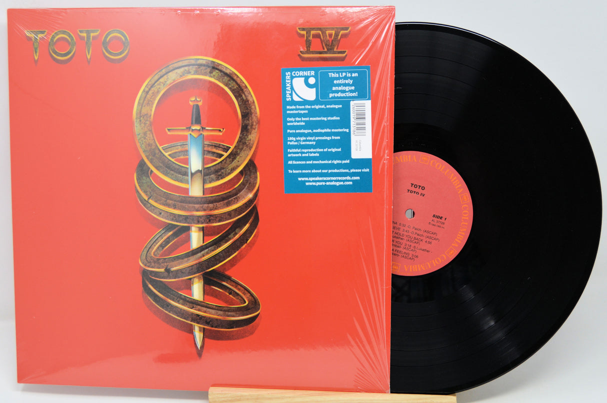 Toto IV vinyl record LP with its red illustrated album cover sleeve and a black vinyl record partially pulled out, photographed on a light gray background.