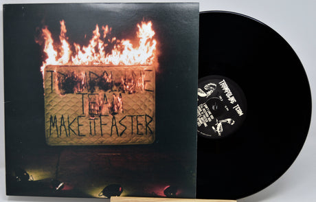 Vinyl record album with the cover partially pulled from the sleeve, showing a black record and a printed cover featuring flames over a textured gold square with the text 'IN A TIME TEAM MAKE IT FASTER'.
