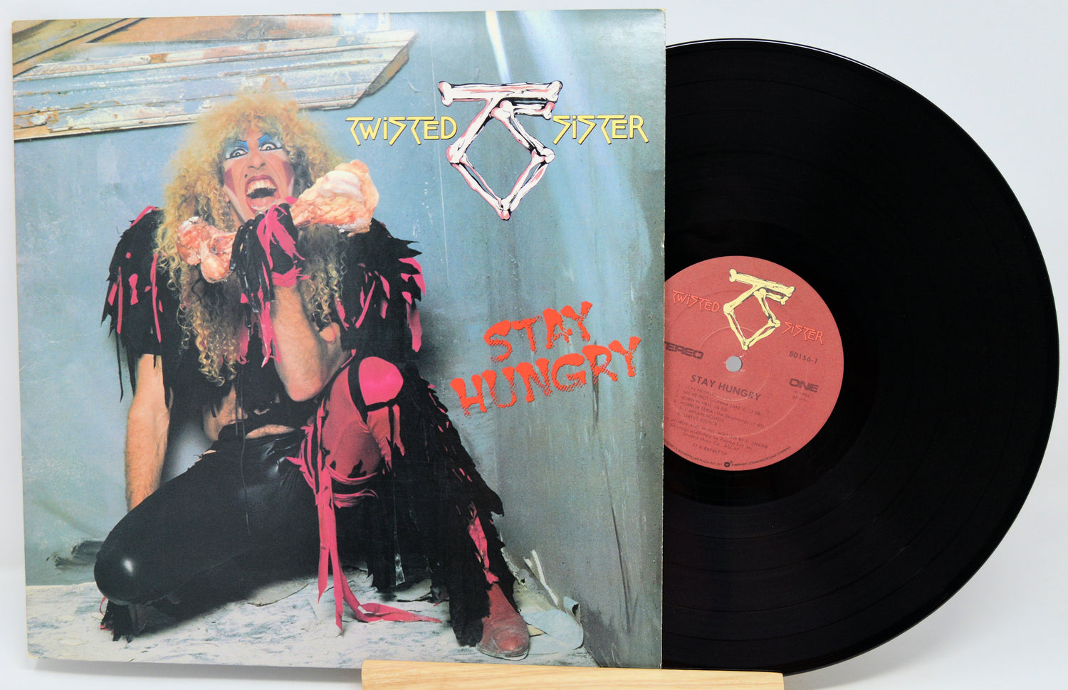Twisted Sister 'Stay Hungry' vinyl record album with the printed cover in front and the black LP record partially pulled out, showing the orange center label.