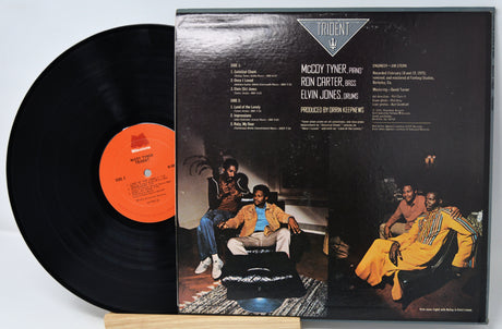 Vinyl record with cover featuring musicians and text on a light gray background