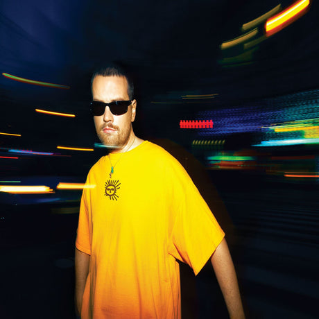 Man wearing a bright yellow t-shirt with sun logo and sunglasses in a neon-lit urban street at night