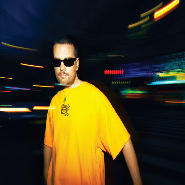Man wearing a bright yellow t-shirt with sun logo and sunglasses in a neon-lit urban street at night