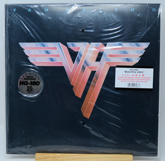 Van Halen II 180g vinyl record in its shrink wrap, featuring the classic metallic 'VH' logo on a black background, with a 'Includes: "Beautiful Girls"' sticker and a 'Vinyl Pressing HQ-180' label.