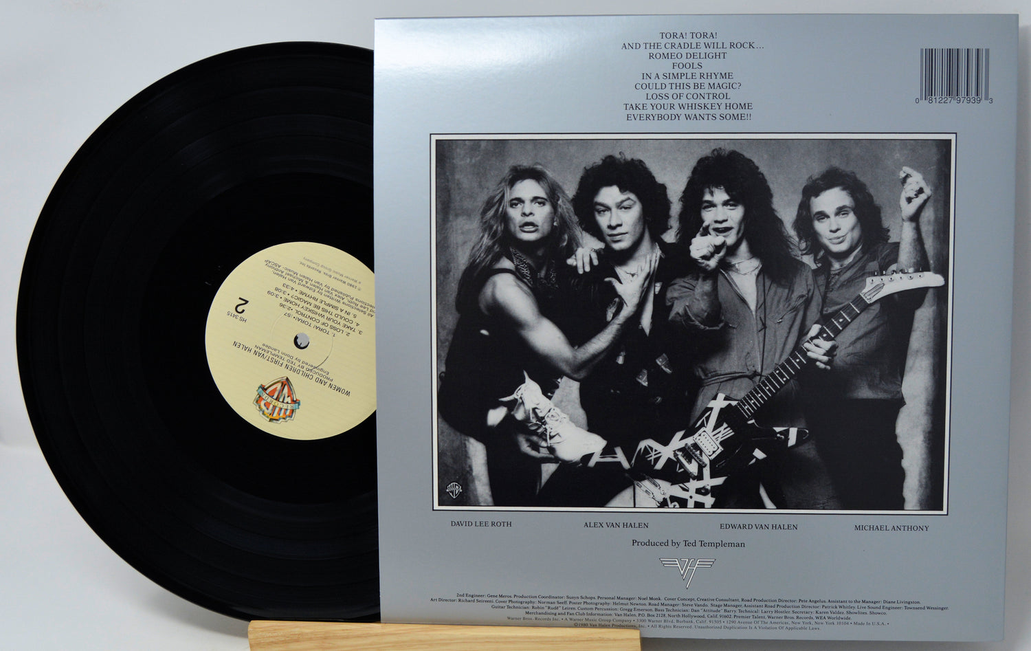 A vinyl record partially pulled from its outer paper sleeve, showing the black record on the left and the back cover with printed tracklist and a black-and-white band photo on the right.